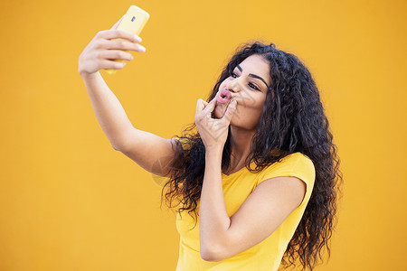 有趣的阿拉伯女人用智能手机拍自拍照片卷发女性年轻的阿拉伯女人用智能手机自拍技术高清图片素材