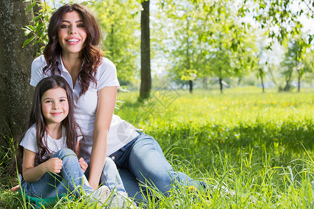 快乐的母亲她的女儿坐公园树下的草地上妈妈女儿公园图片