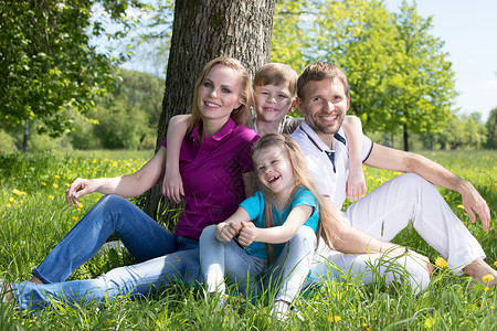 幸福的父母两个孩子坐春天公园的草地上春天公园的家人图片