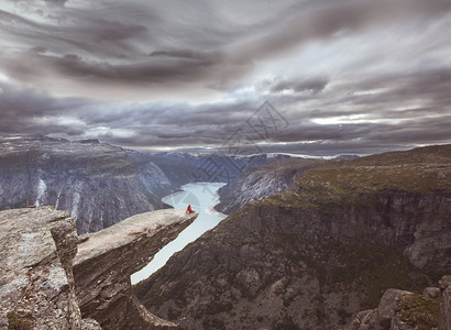 徒步旅行者坐挪威的特罗尔通加悬崖上图片