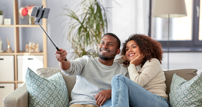 家庭技术人的快乐的非裔美国人夫妇家里用智能手机自拍棒拍照夫妇家里用自拍杆拍照图片