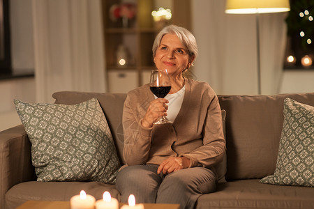 人酒饮料的快乐的高级妇女晚上家里用玻璃喝红酒老年妇女晚上家喝红酒背景图片