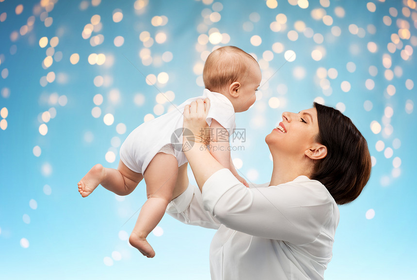 家庭,孩子父母的快乐的微笑中年母亲抱着小宝贝女儿灯光的蓝色背景快乐的中年母亲小女儿图片