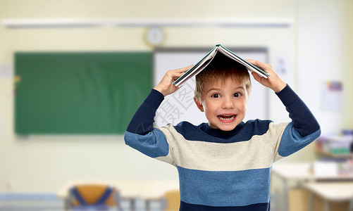 学校,教育学微笑的小男孩,他的头顶上的书教室背景小男孩学校里头顶着书图片