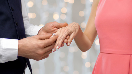 结婚周年素材订婚,求婚人的近距离的男人把钻石戒指戴女人的手指上的假日灯光背景男人把订婚戒指戴女人的手指上背景