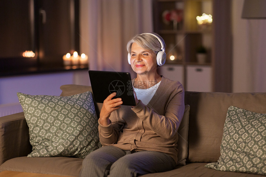 技术,人生活方式的快乐的高级妇女耳机平板电脑电脑家里听音乐晚上戴耳机听音乐的高级女人图片