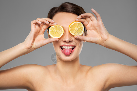逆龄时光美容,护肤排美丽的女人做柠檬片的眼罩,并她的舌头灰色的背景美丽的女人用柠檬片做眼罩背景