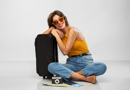 手提箱妇女旅行,旅游度假的快乐的微笑年轻妇女芥末黄色顶部与机票,相机,随身袋灰色背景带旅行袋机票相机的女人背景