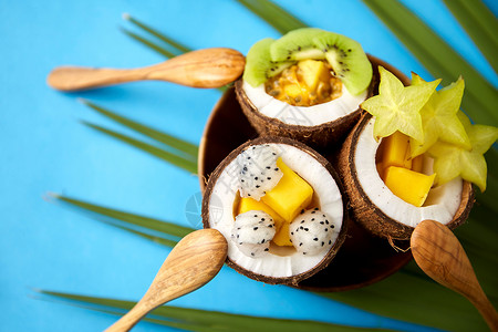 食物,夏天健康的饮食混合同的异国水果椰子壳的盘子与木制勺子绿色风扇棕榈叶蓝色背景用勺子混合椰子壳里的异国水果背景图片