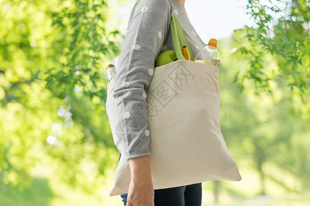 消费主义,饮食生态友好的女与白色可重复用的帆布袋,用于绿色自然背景下的食品购物妇女与可重复用的帆布袋食品购物背景图片