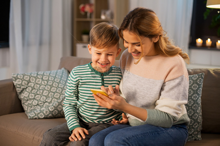 家庭,技术人的快乐的微笑母亲小儿子坐沙发上,家里用智能手机母亲儿子家用智能手机图片