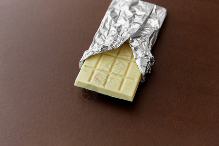 糖果食品白色巧克力棒箔包装棕色背景棕色箔纸包装的白色巧克力图片