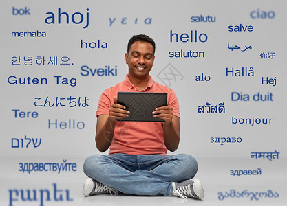 技术,沟通人的快乐的印度男人,平板电脑坐地板上,灰色背景下用同的外语问候语快乐的印度男人与平板电脑背景图片