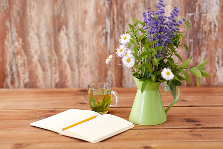 生态有机草药茶,笔记本与铅笔花绿色水壶桌子上凉茶,笔记本桌子上的罐子里的花背景图片
