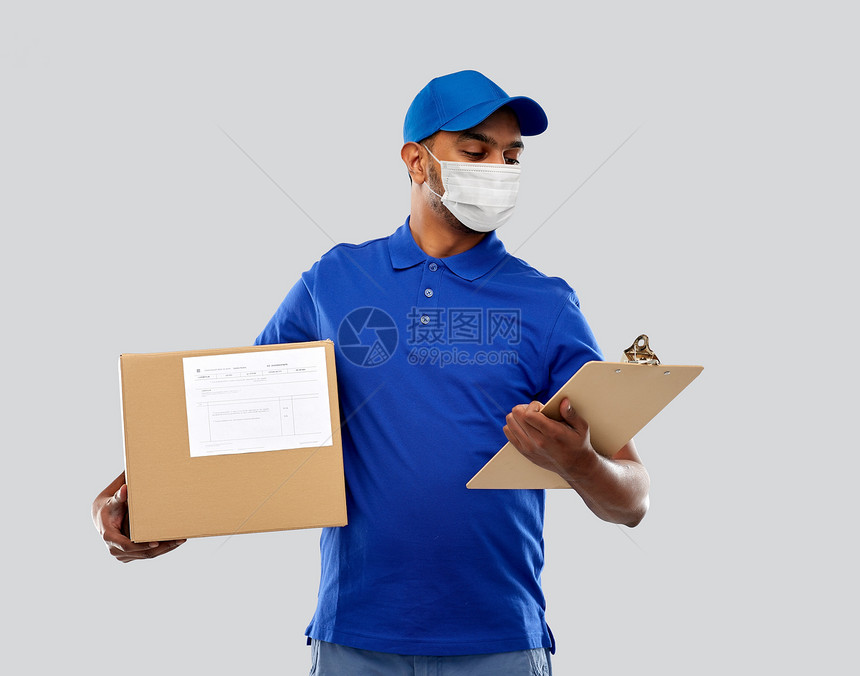 健康安全大流行快乐的印度送货人员戴着面部防护医疗面罩,以防止病疾病,包裹盒剪贴板灰色背景下穿着制服带包裹盒图片
