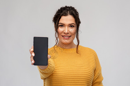刺骨的技术人的快乐的微笑女人展示智能手机灰色背景展示智能手机的快乐女人背景