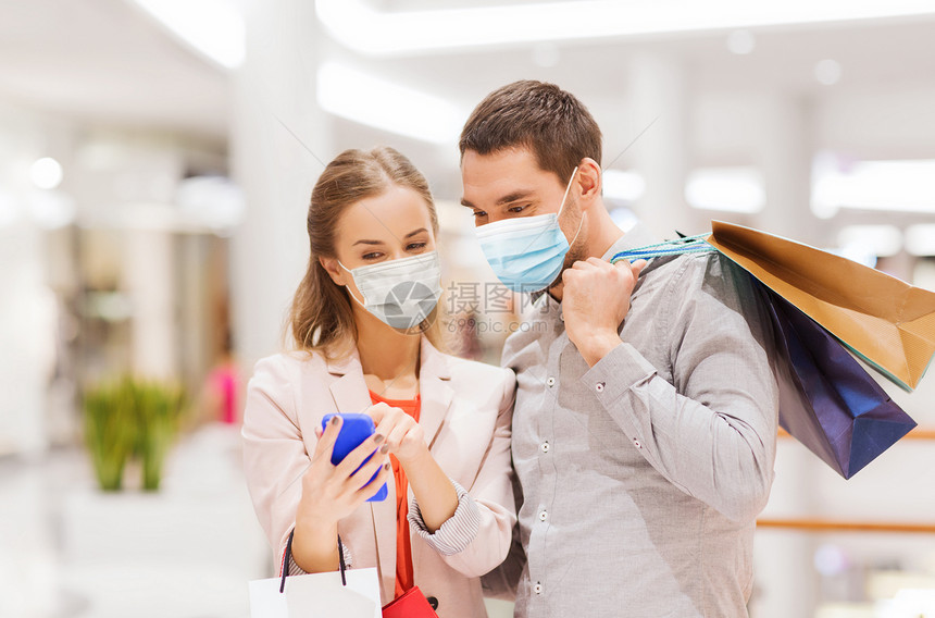 销售,技术流行快乐的年轻夫妇与购物袋智能手机戴着面部保护医学面具,以保护免受病疾病商场戴着面具智能手机的图片