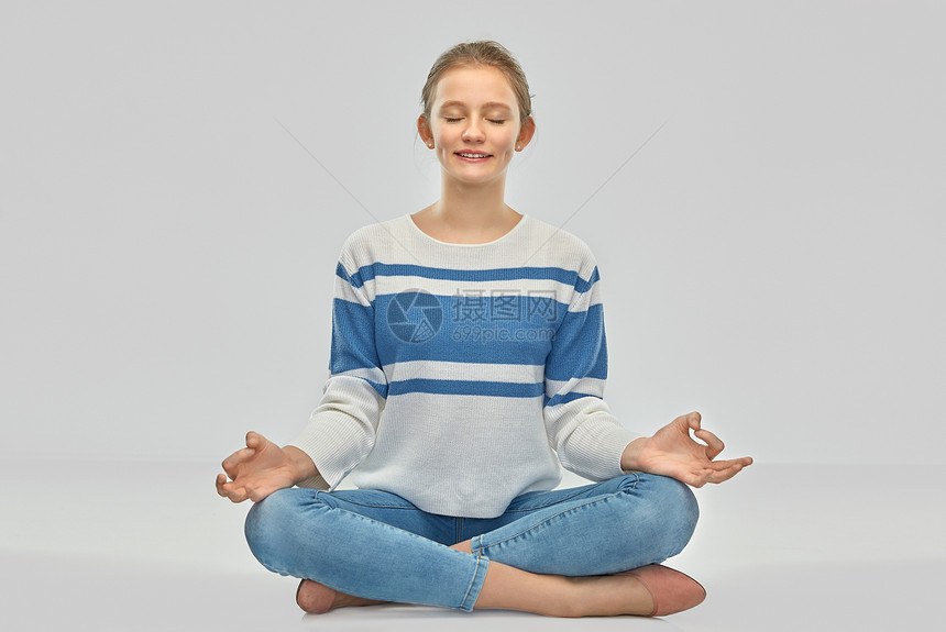 正念,灵人的微笑的十几岁女孩套衫冥想莲花姿势坐地板上灰色的背景微笑的十几岁女孩冥想莲花的姿势图片