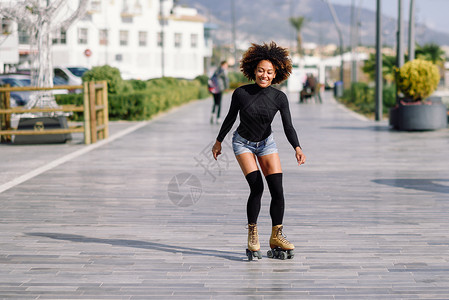 年轻合身的黑人妇女溜冰鞋骑户外的城市街道上阳光明媚的日子里,微笑的女孩留着AFRO的发型骑着溜冰鞋的黑人女人城市街背景图片