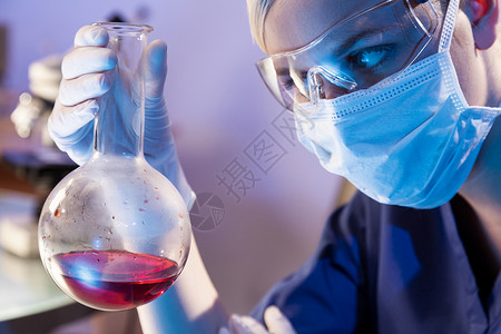 女科学家医学或科学研究员或医生实验室里看着瓶红色的溶液,实验室的设备她身后失去了焦点背景图片