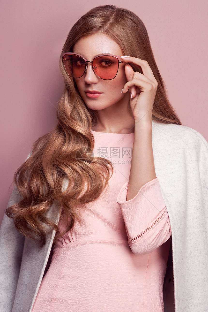 年轻优雅的女人穿着时髦的白色外套金发,粉红色连衣裙,演播室镜头时尚秋季看书戴太阳镜的模特儿图片
