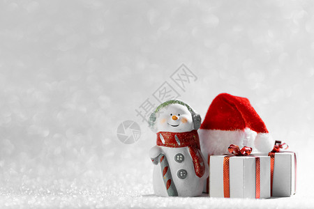 带圣诞帽雪人圣诞快乐新年贺卡快乐的雪人站圣诞礼物圣诞老人的帽子上银色的闪光背景带圣诞礼物圣诞帽的雪人背景