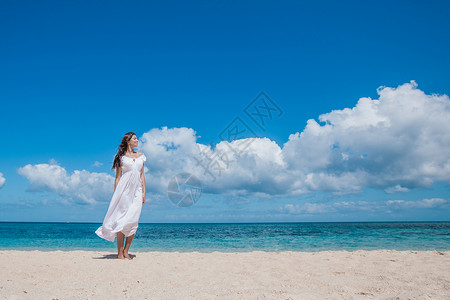 穿着白色连衣裙的年轻女人沿着沙滩漫步女人沿着海滩散步图片
