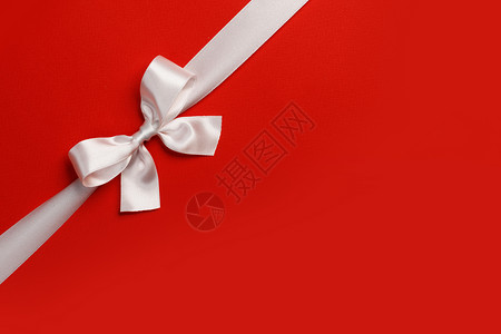 白色礼品蝴蝶结红色背景下,用于文字节日礼物的白色礼物蝴蝶结红色图片
