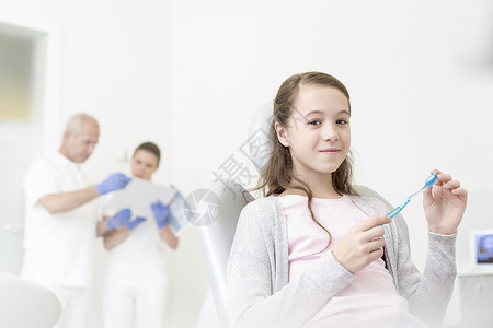 微笑的女孩着牙刷,坐诊所里抗医生背景