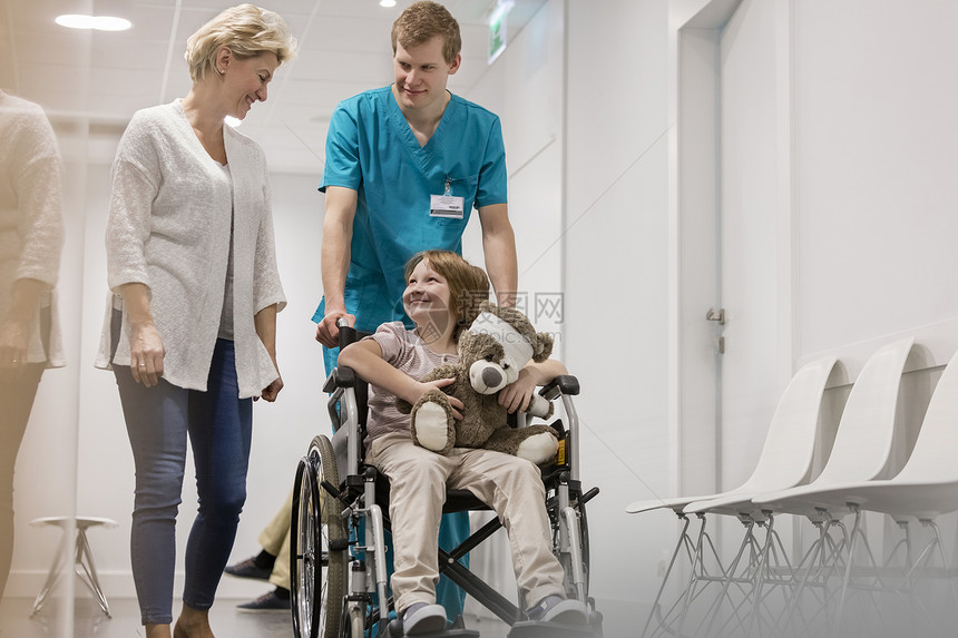母亲护士起散步,把生病的男孩推医院走廊的轮椅上图片