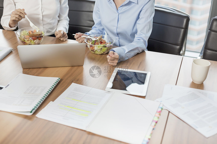 中层的女商人会议室里坐桌子旁吃午饭图片