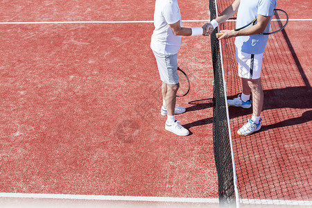 比赛中,红场上站网球网旁的低段男子握手图片