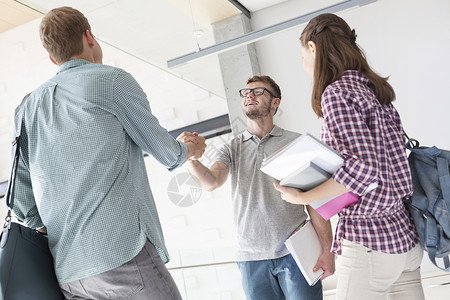女人看着朋友大学走廊里握手问候男人高清图片素材