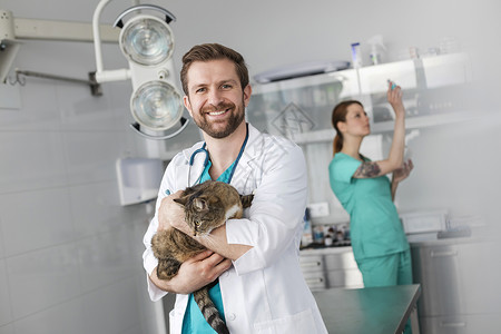 诊所面同事时,微笑的兽医医生带着猫的肖像背景图片