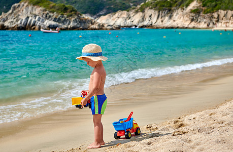 带草帽的男孩两岁的蹒跚学步的男孩海滩上带着玩具戴着草帽的孩子暑假家庭假期希腊西索尼亚背景