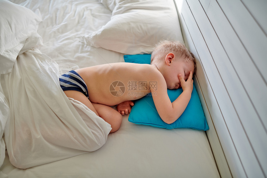 三岁的蹒跚学步的男孩睡毯子下的蓝色枕头上图片