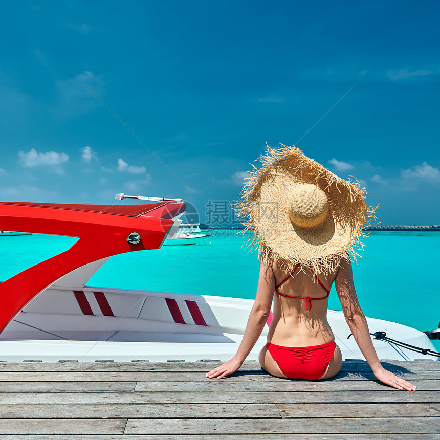 穿着红色比基尼的女人坐木船码头上马尔代夫的暑假图片