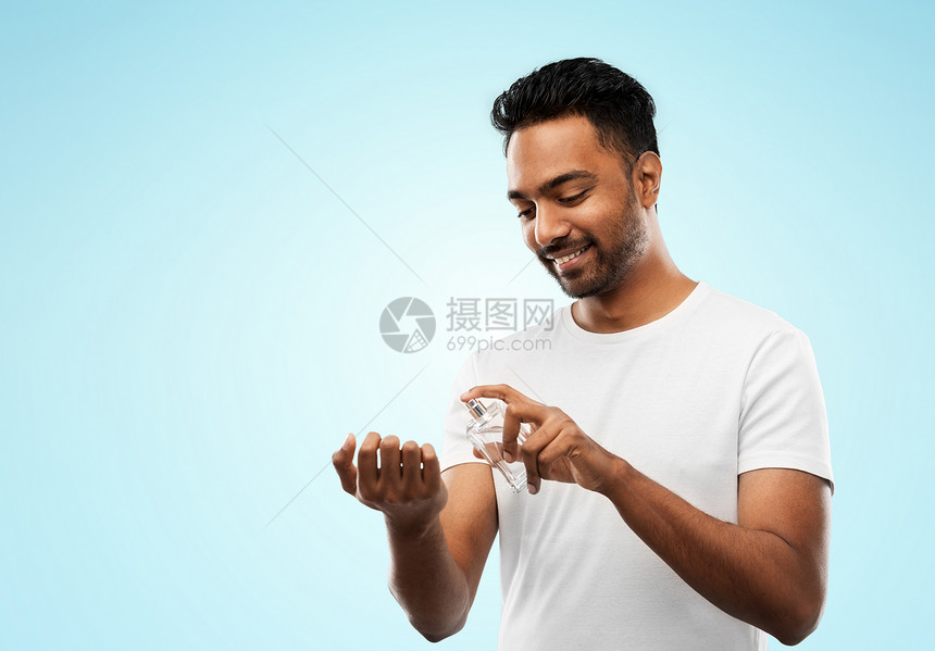 男香水,修饰人的快乐微笑的轻印度男子喷香水他的手腕上蓝色的背景快乐的印度男人用蓝色背景的香水图片
