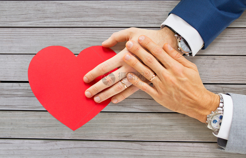 ,同婚姻,情人节爱情亲密的幸福已婚男夫妇的手与红纸心形的桌子上密切的男夫妇的手与红色的心图片
