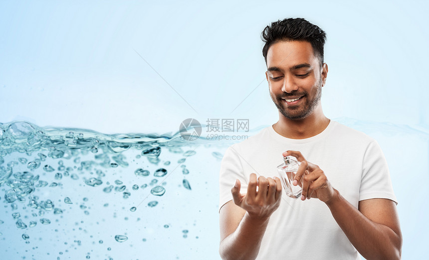 男香水,修饰人的快乐微笑的轻印度男子喷香水他的手腕上蓝色的背景快乐的印度男人用蓝色背景的香水图片