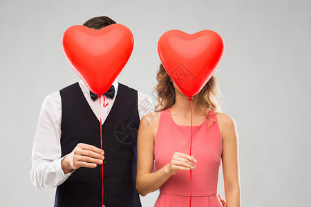 情人节,爱人的夫妇隐藏红色心形气球后的灰色背景夫妇躲红色心形气球后图片