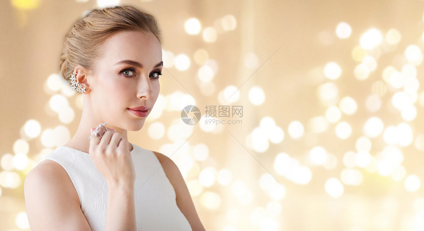 珠宝,奢侈品人的白色连衣裙的女人肖像与钻石耳环指环米色背景节日灯穿着白色连衣裙带钻石珠宝的女人图片