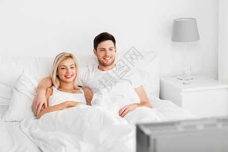 人,休闲休息的幸福的夫妇躺家里的床上看电视幸福的夫妇躺家里的床上看电视图片