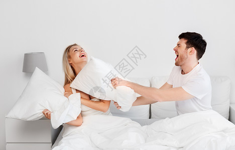 人们趣的快乐的夫妇家里床上打枕头战幸福的夫妇床上打枕头战背景