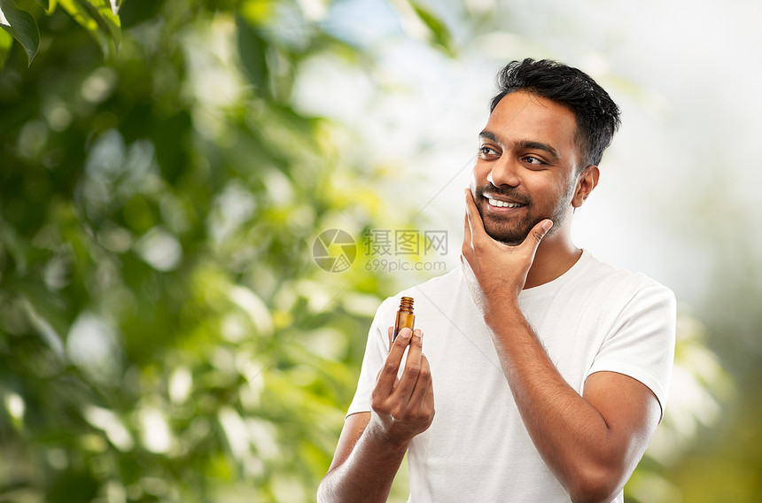 美容人的微笑的轻印度男子应用乳液胡须油绿色的自然背景微笑的印度男人胡须上涂上美容油图片