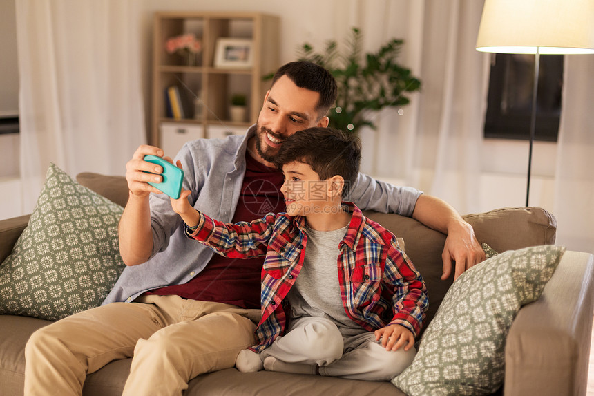 人,家庭技术快乐的父亲小儿子坐家里的沙发上用智能手机自拍父子家里自拍图片