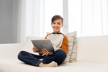 童,技术人的微笑的男孩与平板电脑坐沙发上家微笑的男孩家里用平板电脑电脑图片