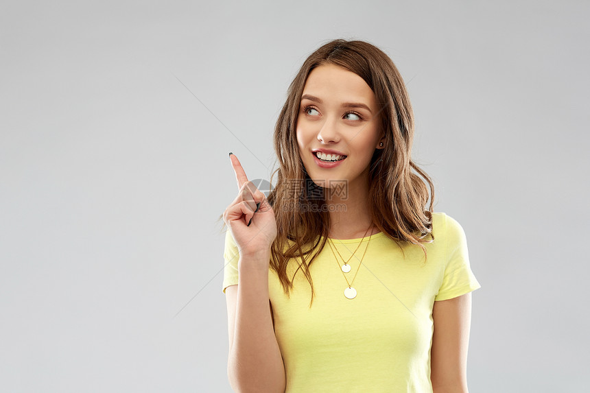 人们的微笑的轻女人十几岁的女孩穿着空白的黄色T恤,手指指向灰色背景轻的女人十几岁的女孩竖手指图片