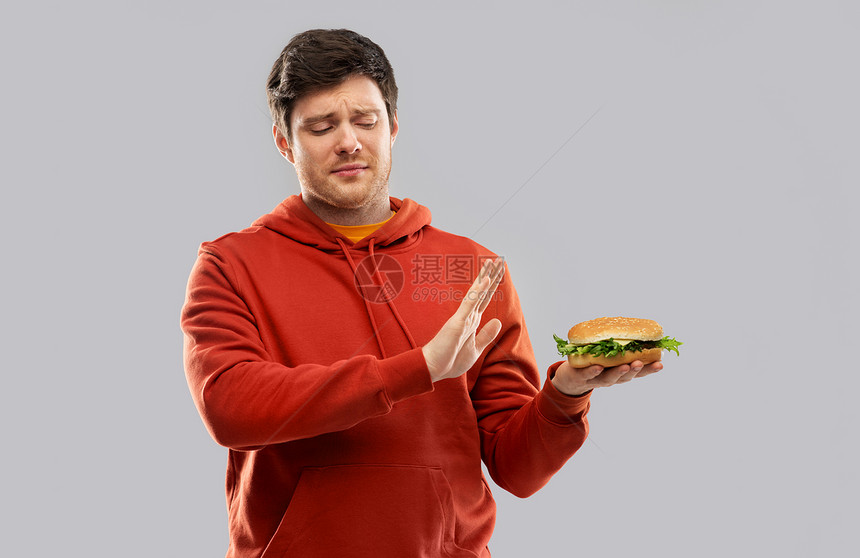 快餐,健康的饮食人们的观念穿着红色帽衫的轻人拒绝灰色背景下吃汉堡包轻人拒绝汉堡包图片