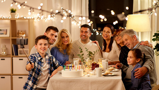 生日拍照庆祝,假日人们的幸福的家庭家里举行生日茶会,并自拍杆上用智能手机拍照家庭生日派自拍背景